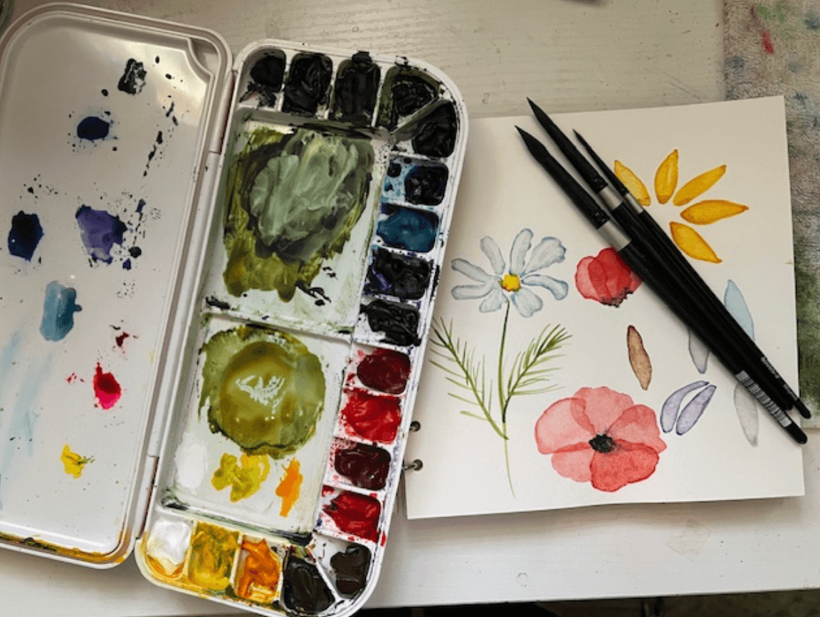 Artist's work area with palette, paint, brushes and sketchbook.